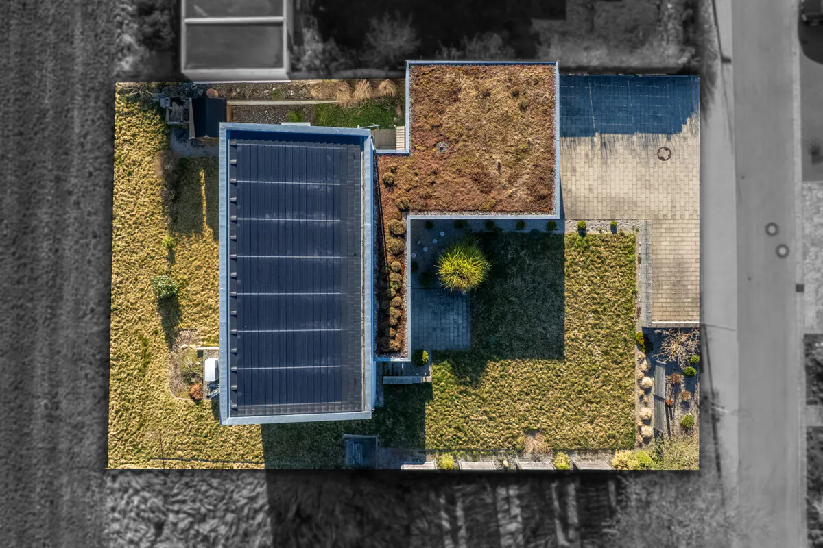 Aerial view of a modern house with a black roof, a green roof, and a green lawn.