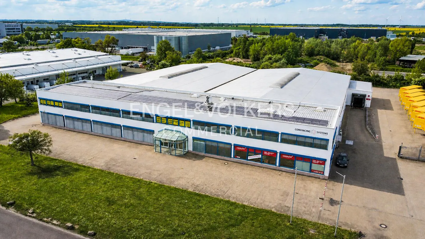 Aerial view of a two-story white commercial building with a gray roof and blue trim. "Engel & Volkers Commercial" is displayed on the building.