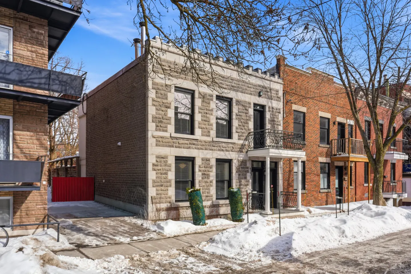 Exterior view of a two-story stone house with black windows and a small balcony, snow on the ground.