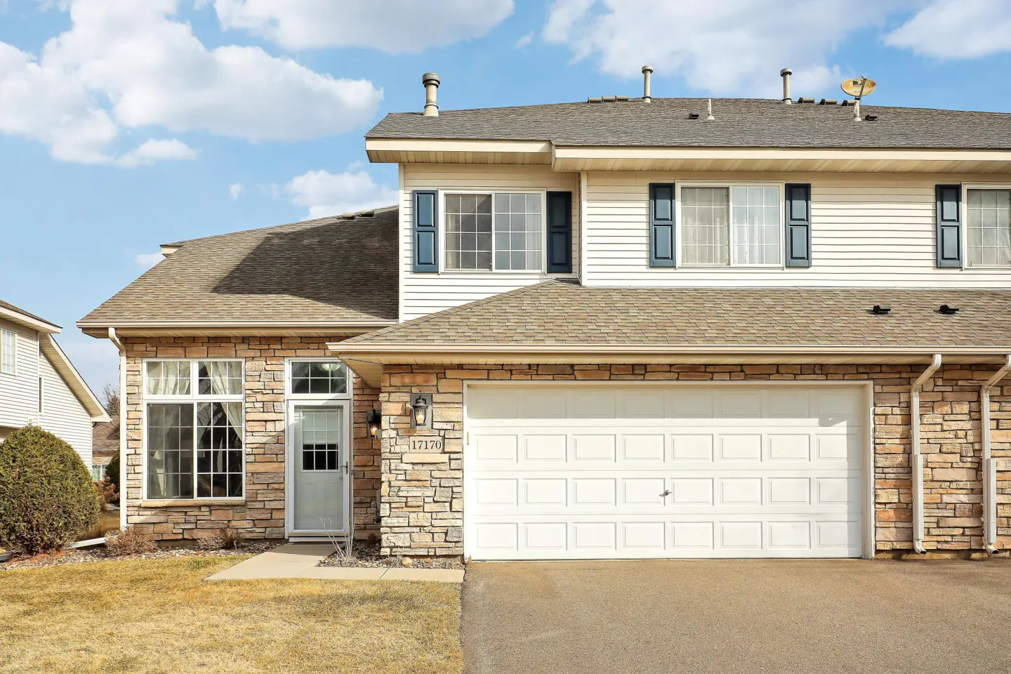 Exterior of a two-story townhouse with stone and white siding, a two-car garage, and blue shutters.