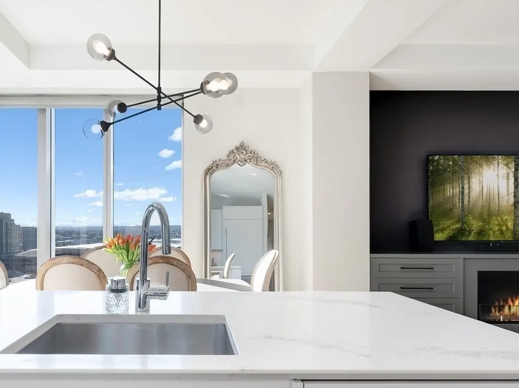 A modern kitchen with a white countertop, stainless steel sink, and a view of the city skyline through a large window.