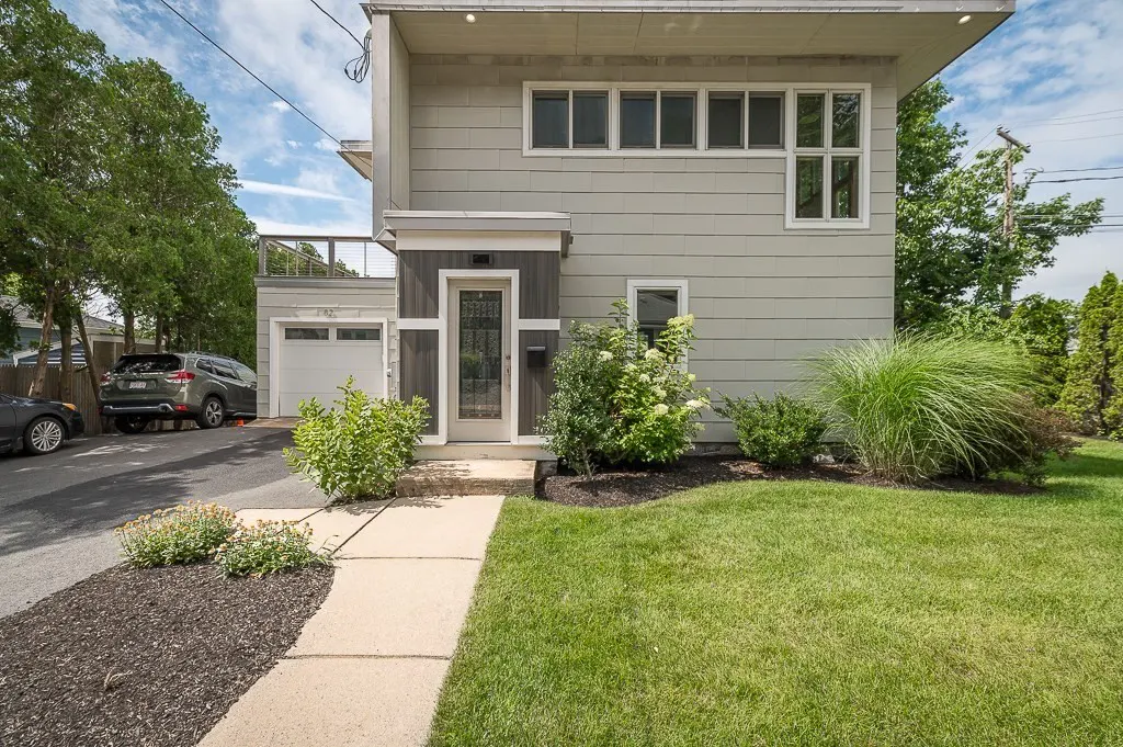 Modern two-story grey house with a white front door, concrete walkway, green lawn, and a driveway with a parked SUV.