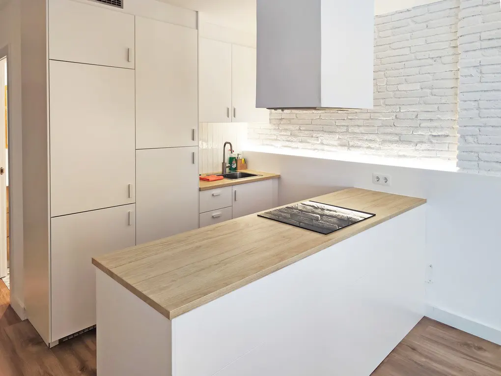 Bright kitchen with white cabinets, wood countertop island with cooktop, and white brick wall.