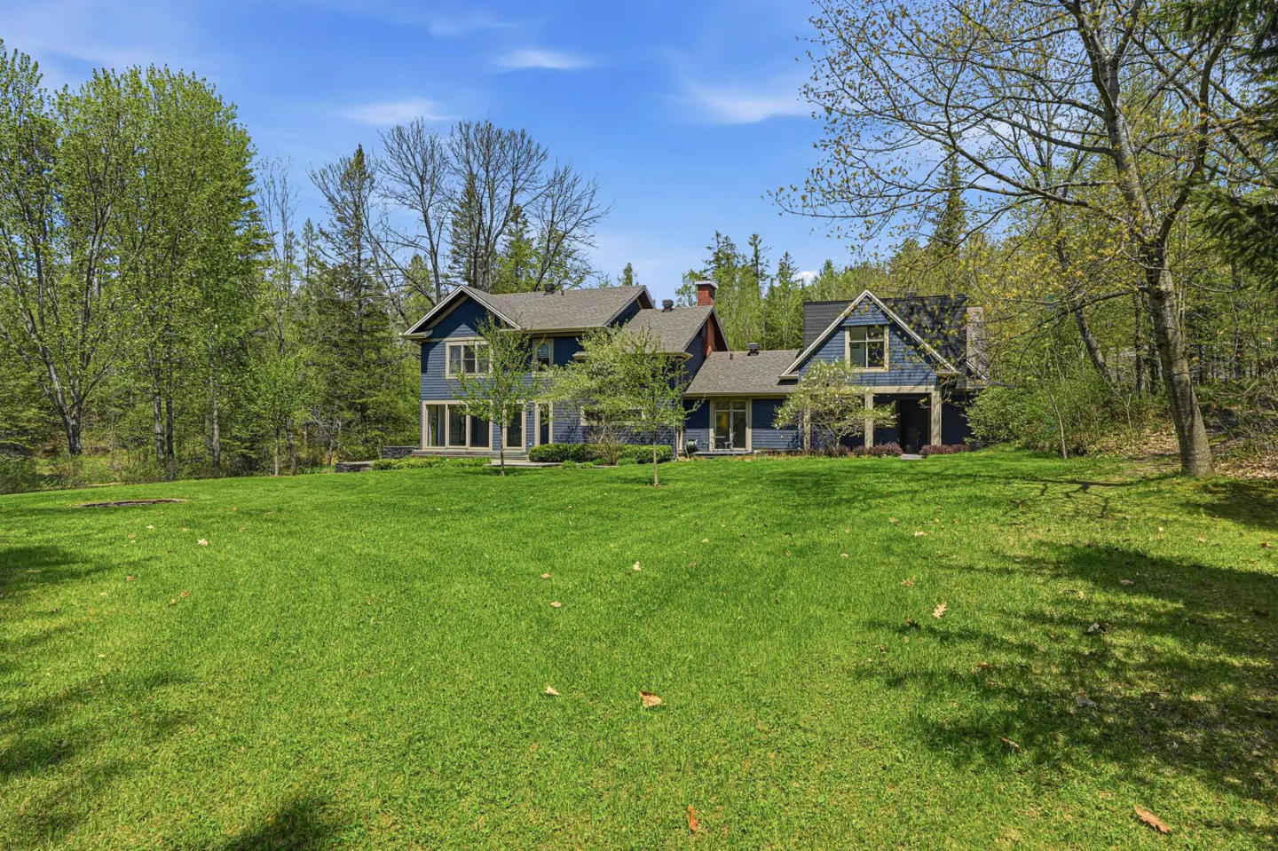 A blue two-story house with a large green lawn and trees in the background.