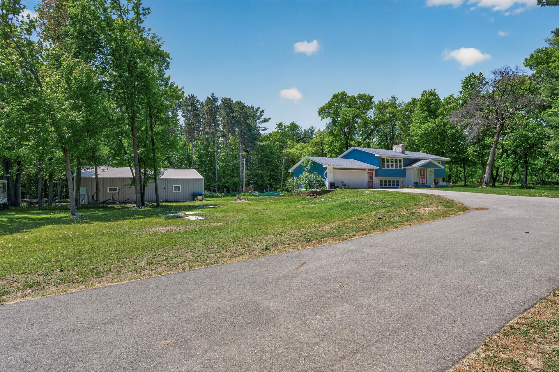 Exterior view of a blue and white house with a gray driveway and a gray shed surrounded by green trees.