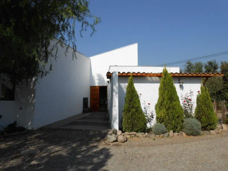 Modern white house with a brown door, green trees, and a gravel driveway under a clear blue sky.