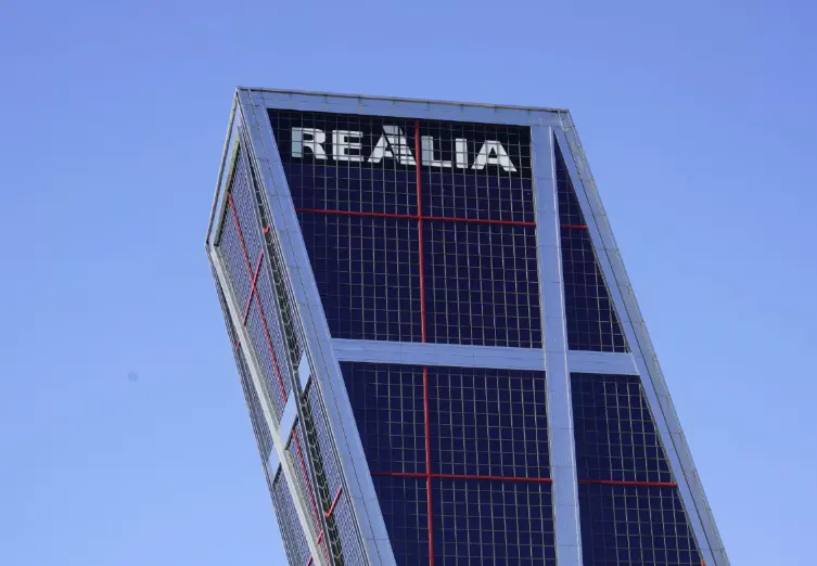 Low angle view of the tilted KIO Towers building in Madrid, Spain, with "REALIA" at the top, against a clear blue sky.