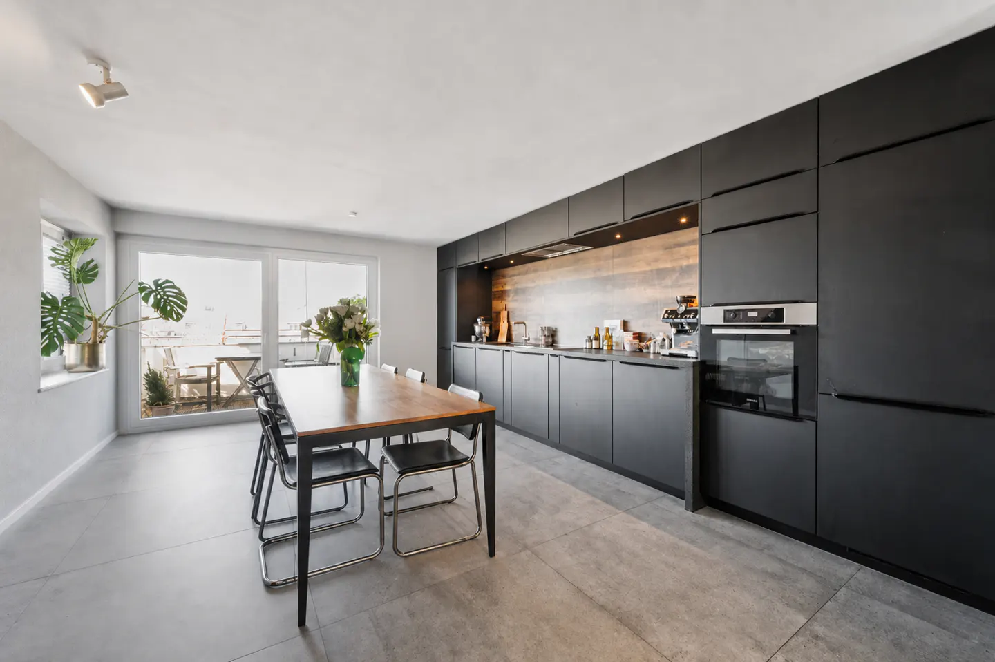 A modern kitchen with black cabinets, a wooden table with chairs, and a view from the window.