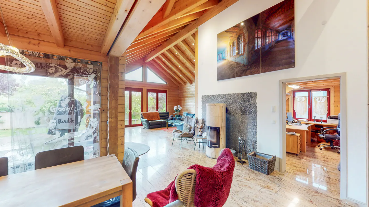 A bright, open-concept living room with wood beams, a stone fireplace, and a large window with a view of the outdoors.