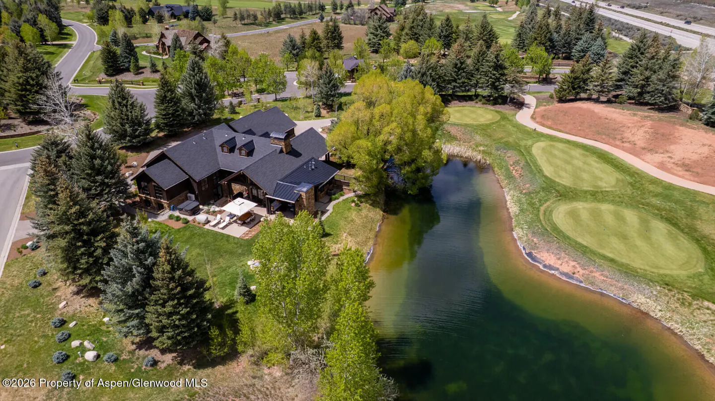 Aerial view of a brown house with a black roof next to a pond and golf course.