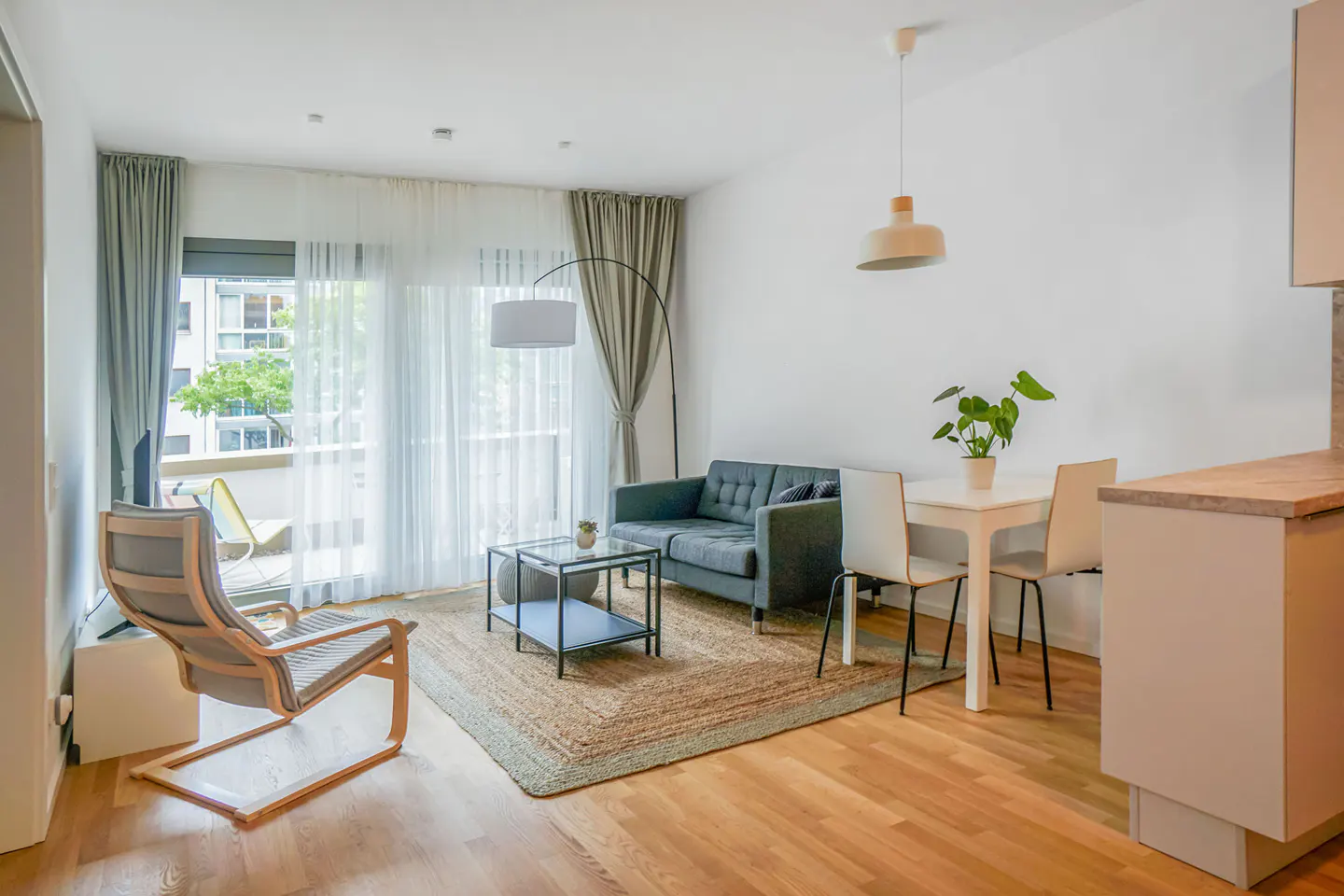 Bright living room with wood floors, a gray sofa, a jute rug, and a balcony with sheer curtains.