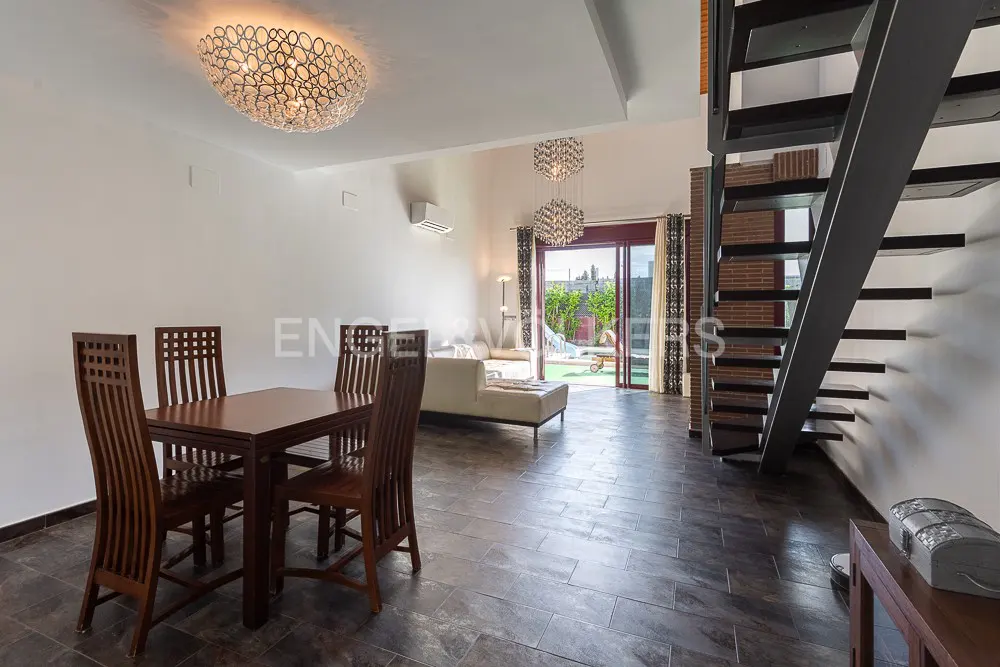 Open-concept living space with a dark wood dining set, modern chandeliers, and a black staircase leading to the upper level. Sliding glass doors open to a patio.