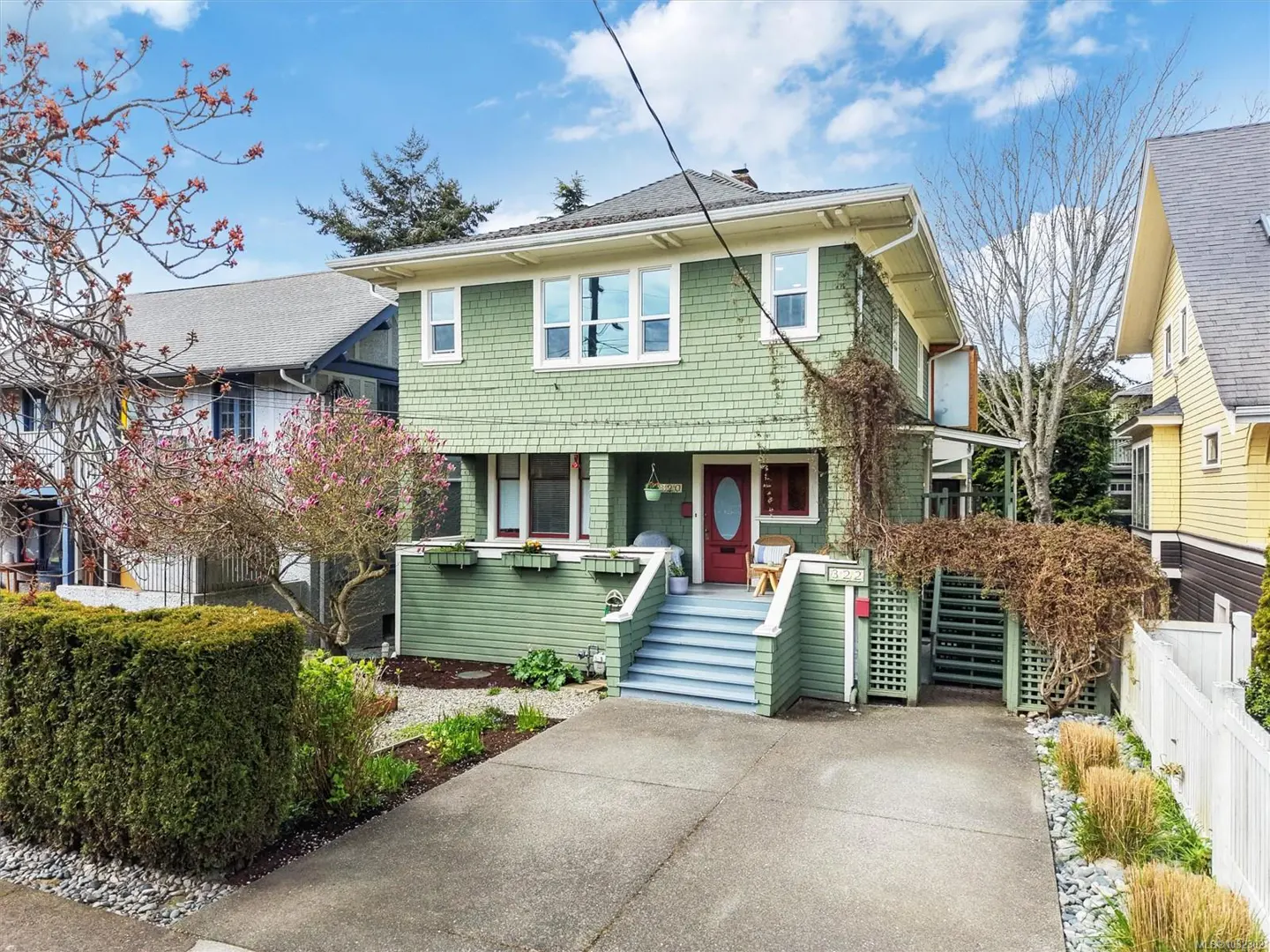 Two-story green house with a red front door and blue stairs. A concrete driveway leads up to the house.