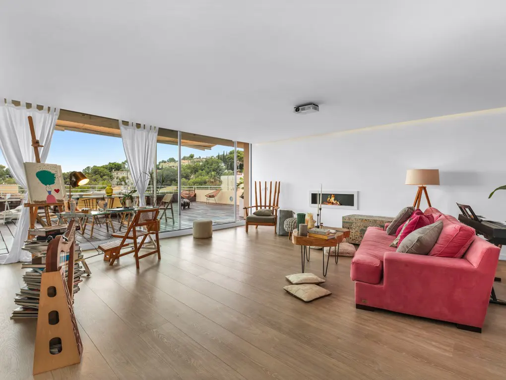 Bright, modern living room with wood floors, pink couch, fireplace, and balcony with easel and outdoor seating.