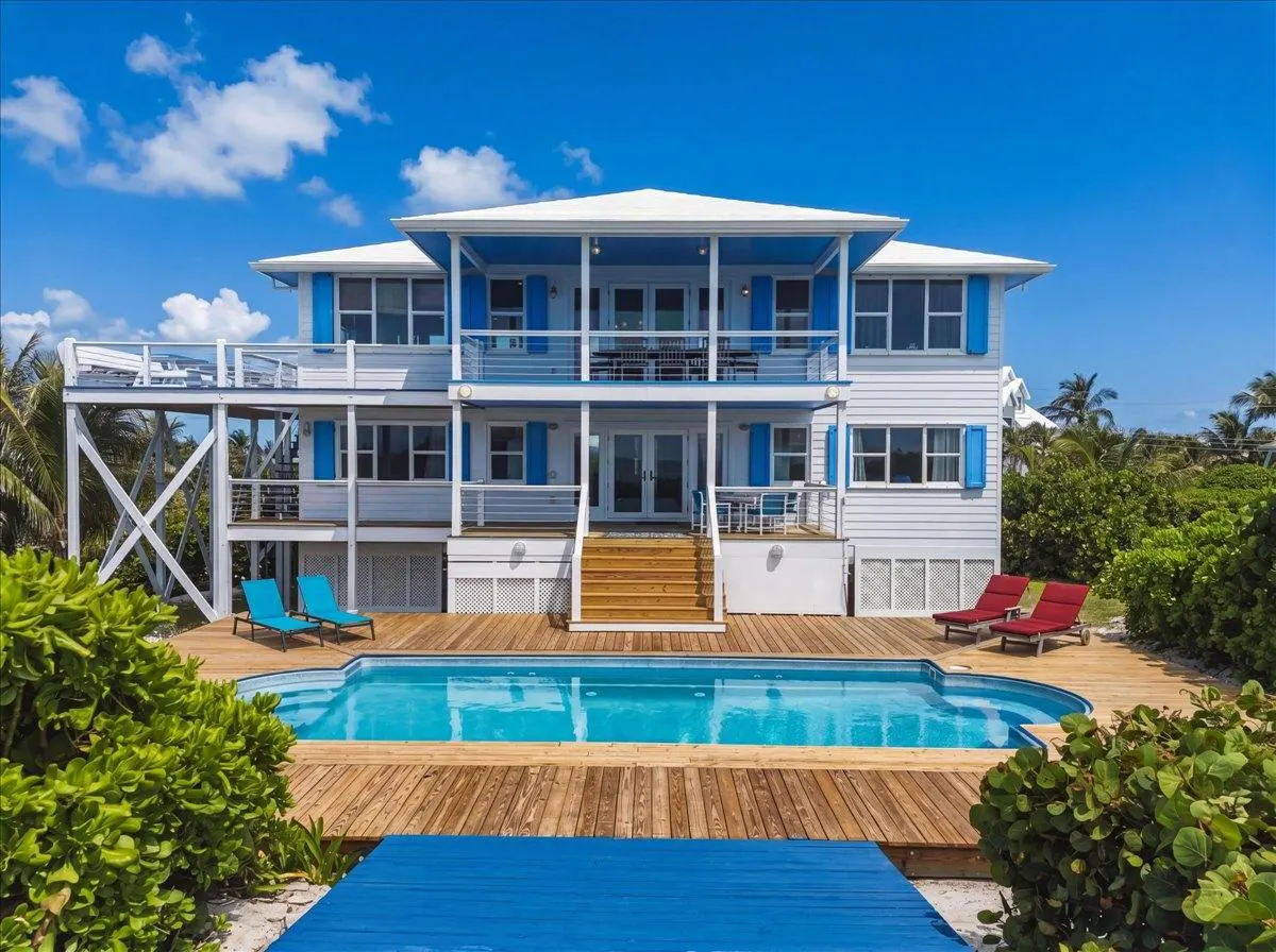 Two-story white house with blue shutters, a pool, and a wooden deck on a sunny day.