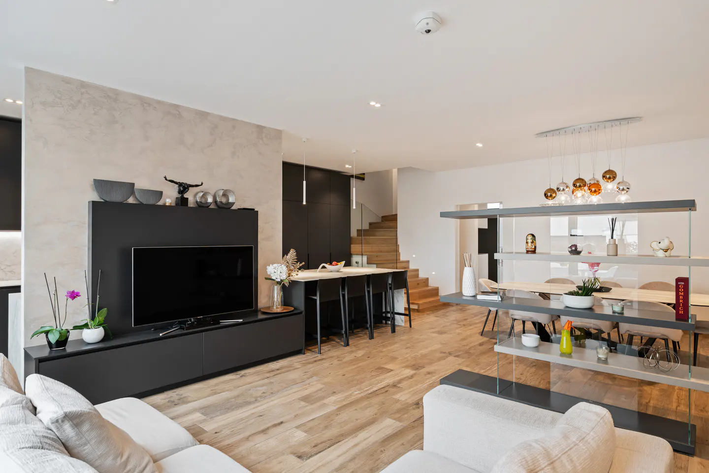 Open-concept living space with a black TV console, island with stools, and a dining area with a decorative shelf.