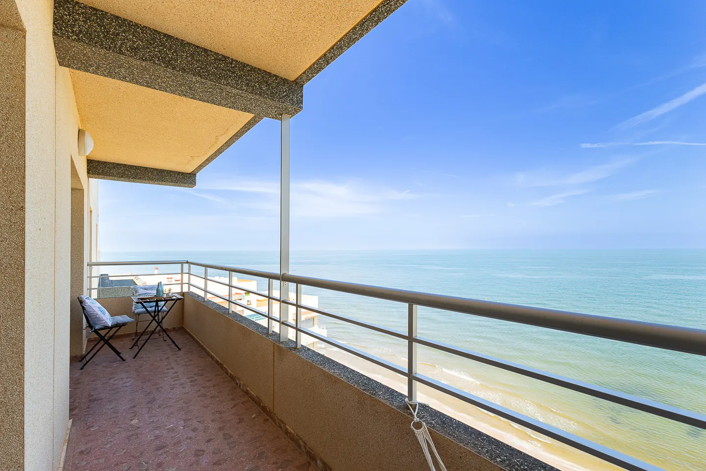 Balcony view of the ocean. Two chairs and a small table sit on the red tiled balcony overlooking the blue ocean and sky.