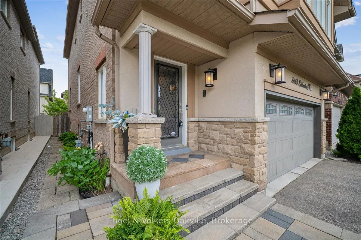 Front entrance of a suburban home with stone accents, a grey garage door, potted greenery, and a paved walkway.