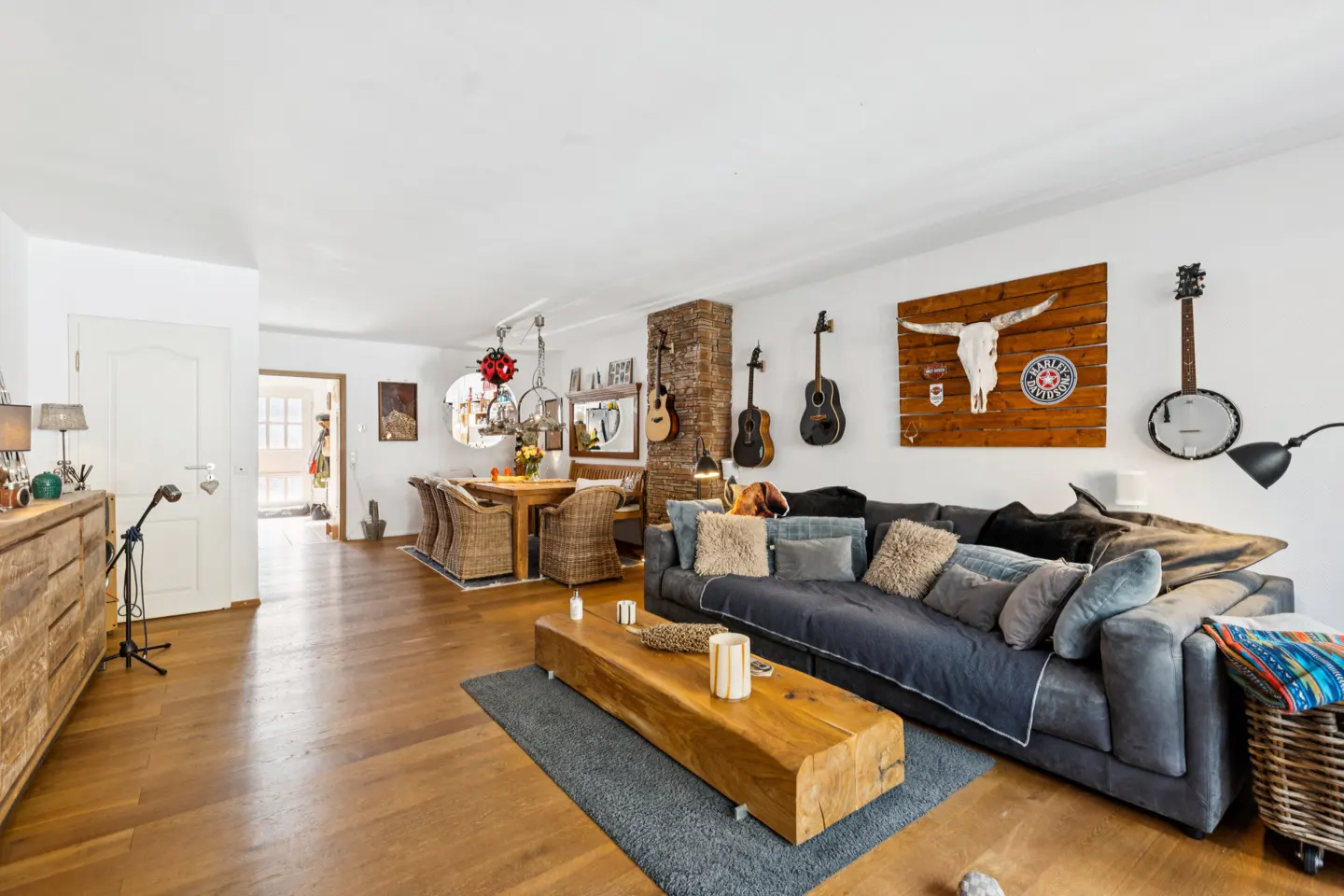 A living and dining area with hardwood floors, a gray sofa, and guitars on the wall.