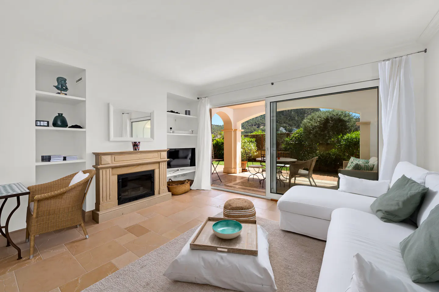 Bright living room with white sofa, fireplace, and sliding glass doors to a patio with outdoor seating.