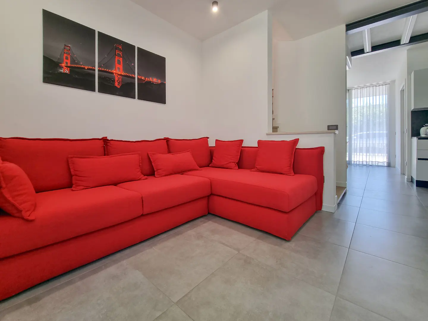 Living room with a large red sectional sofa, gray tile floor, and a triptych of the Golden Gate Bridge on the white wall.