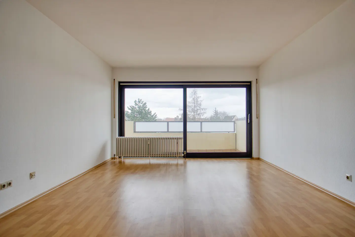 Empty room with wood floor, white walls, radiator, and sliding glass door to a balcony.