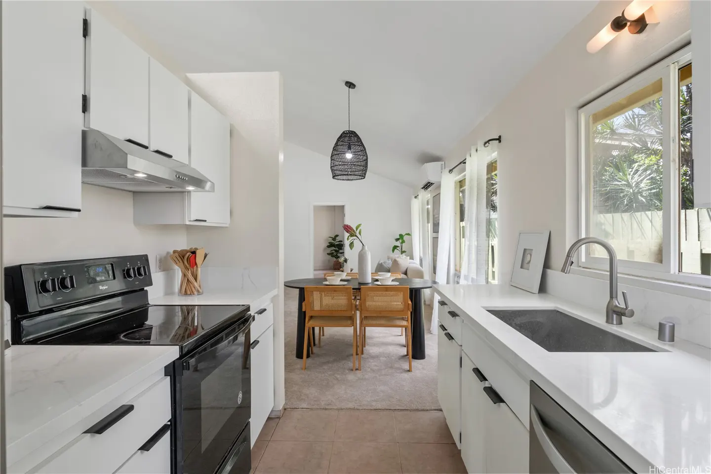 A bright kitchen with white cabinets, countertops, and a black stove. A dining table with chairs is visible in the background.