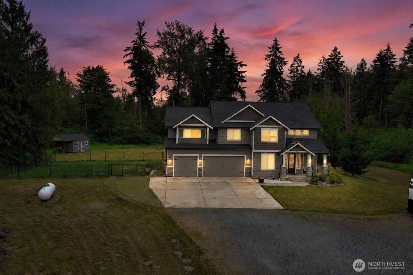 Two-story gray house with a black roof, two-car garage, and a pink and purple sunset sky.