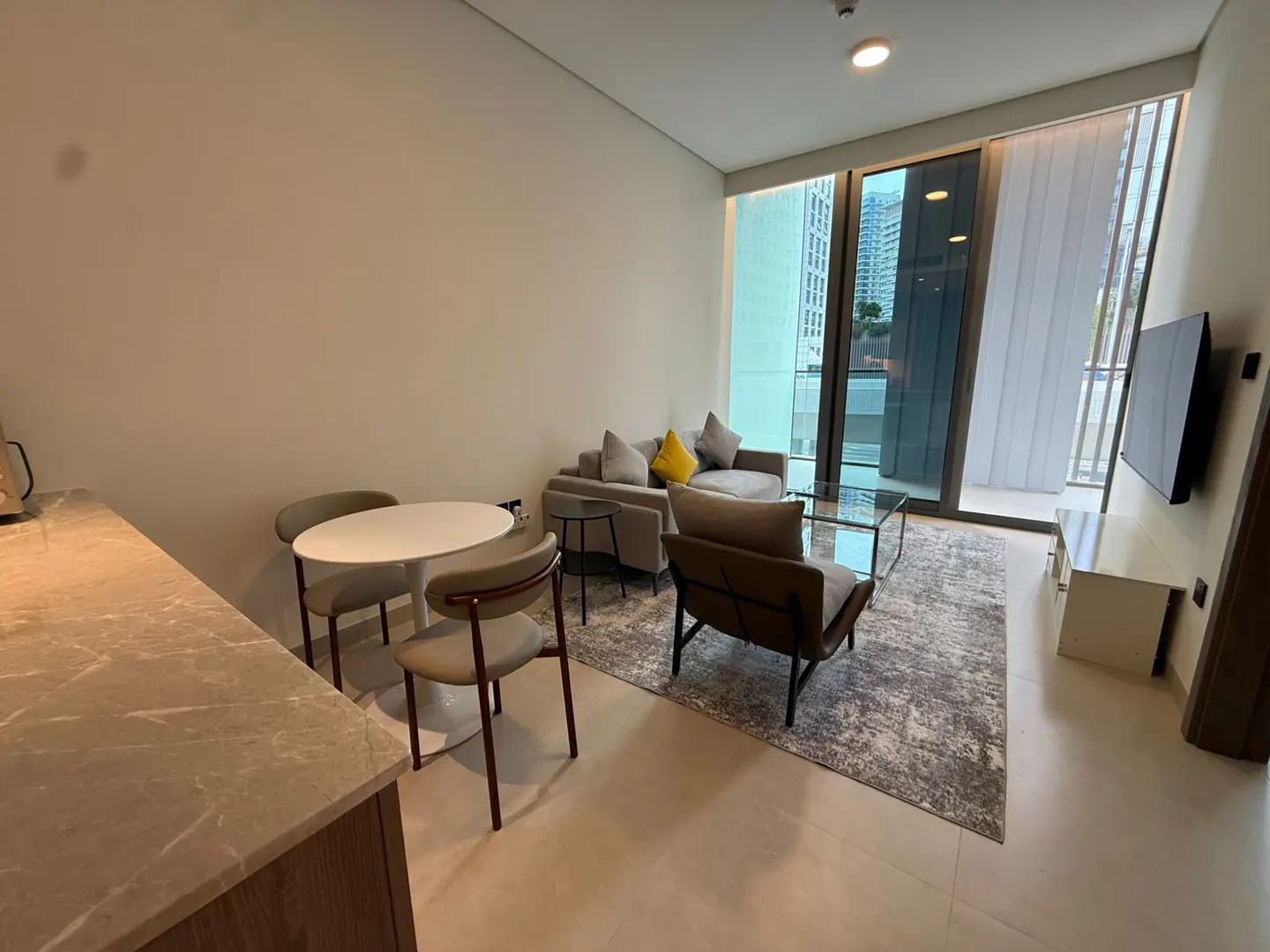 A modern apartment interior with a dining table, sofa, armchair, and a large window.