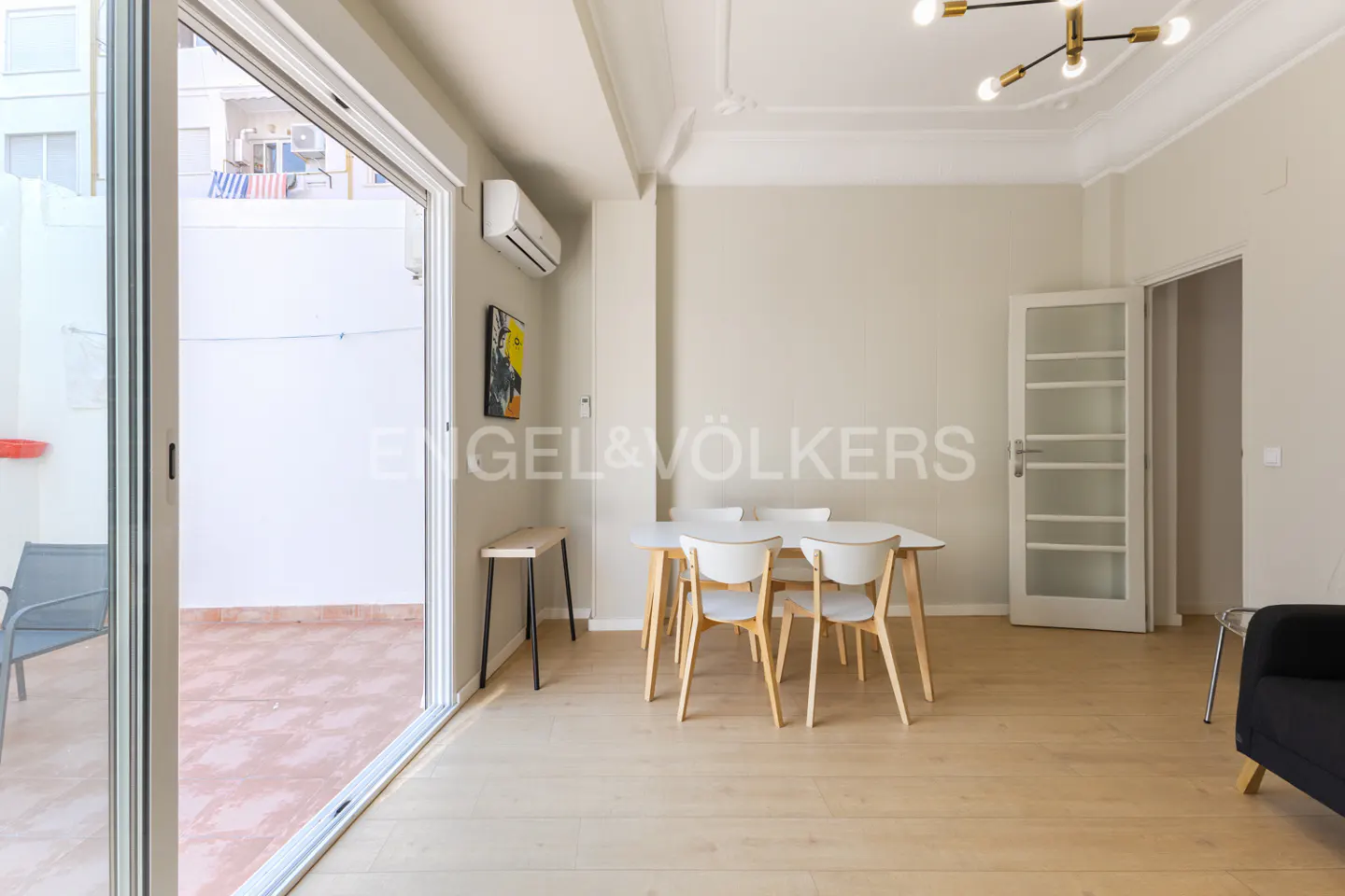 Bright apartment interior with a white table and chairs, light wood floors, and a sliding glass door to a patio.