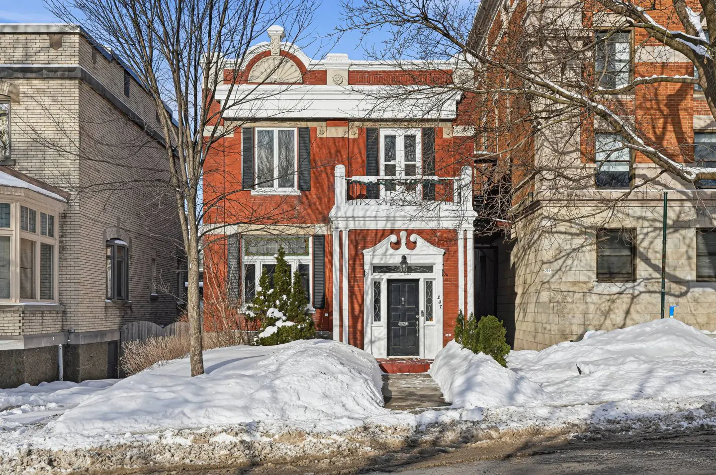 Two-story red brick house with white trim and black shutters, surrounded by snow in winter.