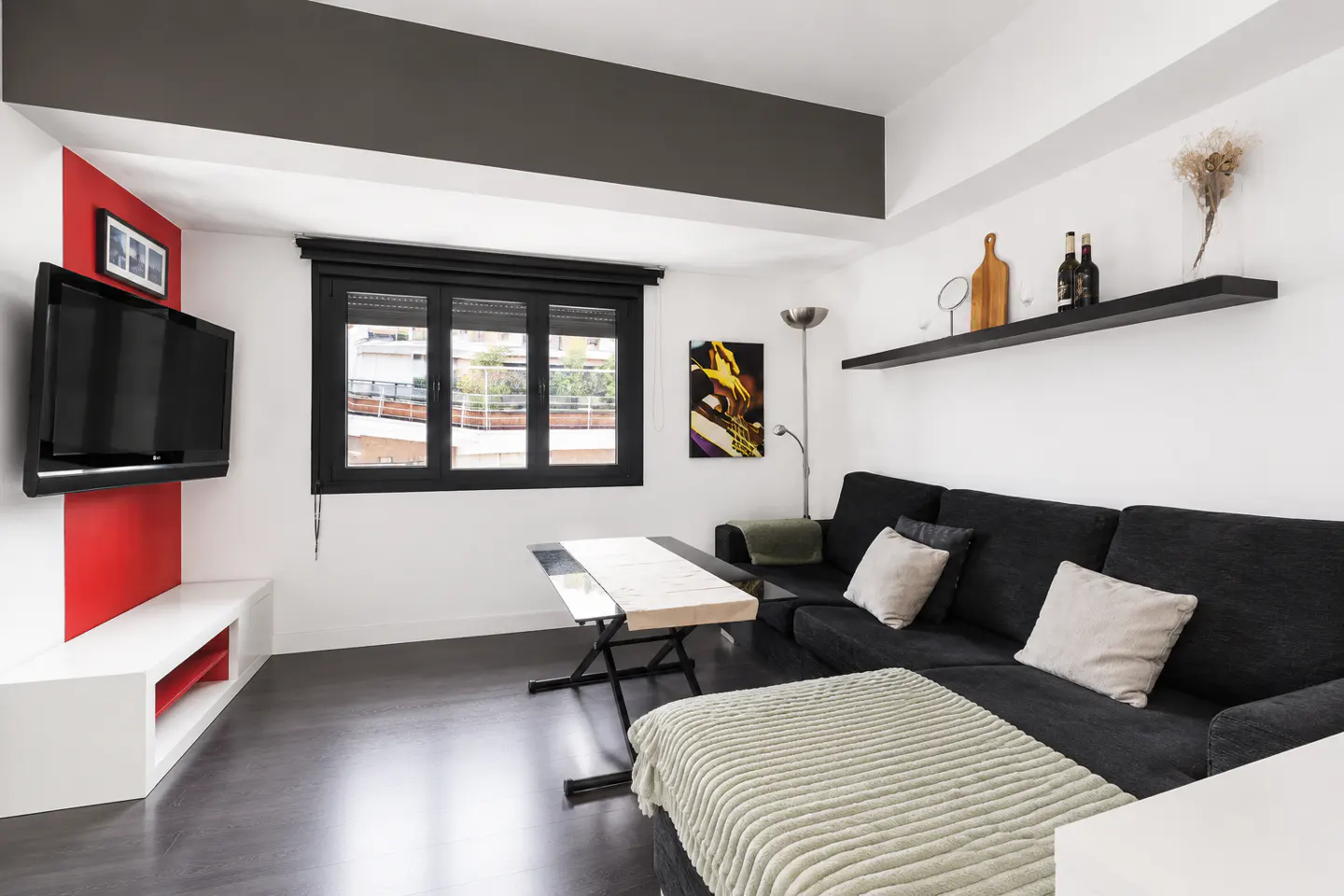 Living room with a black sofa, a table, and a TV on a red and white wall. A black shelf holds decor.