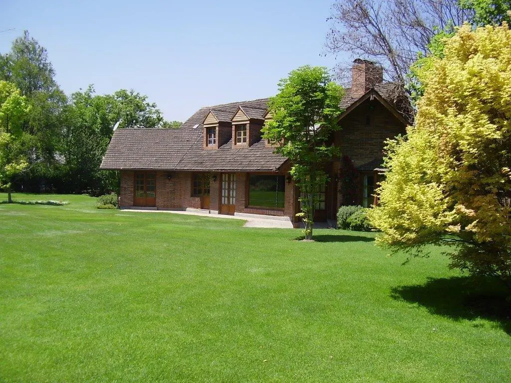 Brick house with a brown roof and dormer windows, surrounded by a large green lawn and trees.