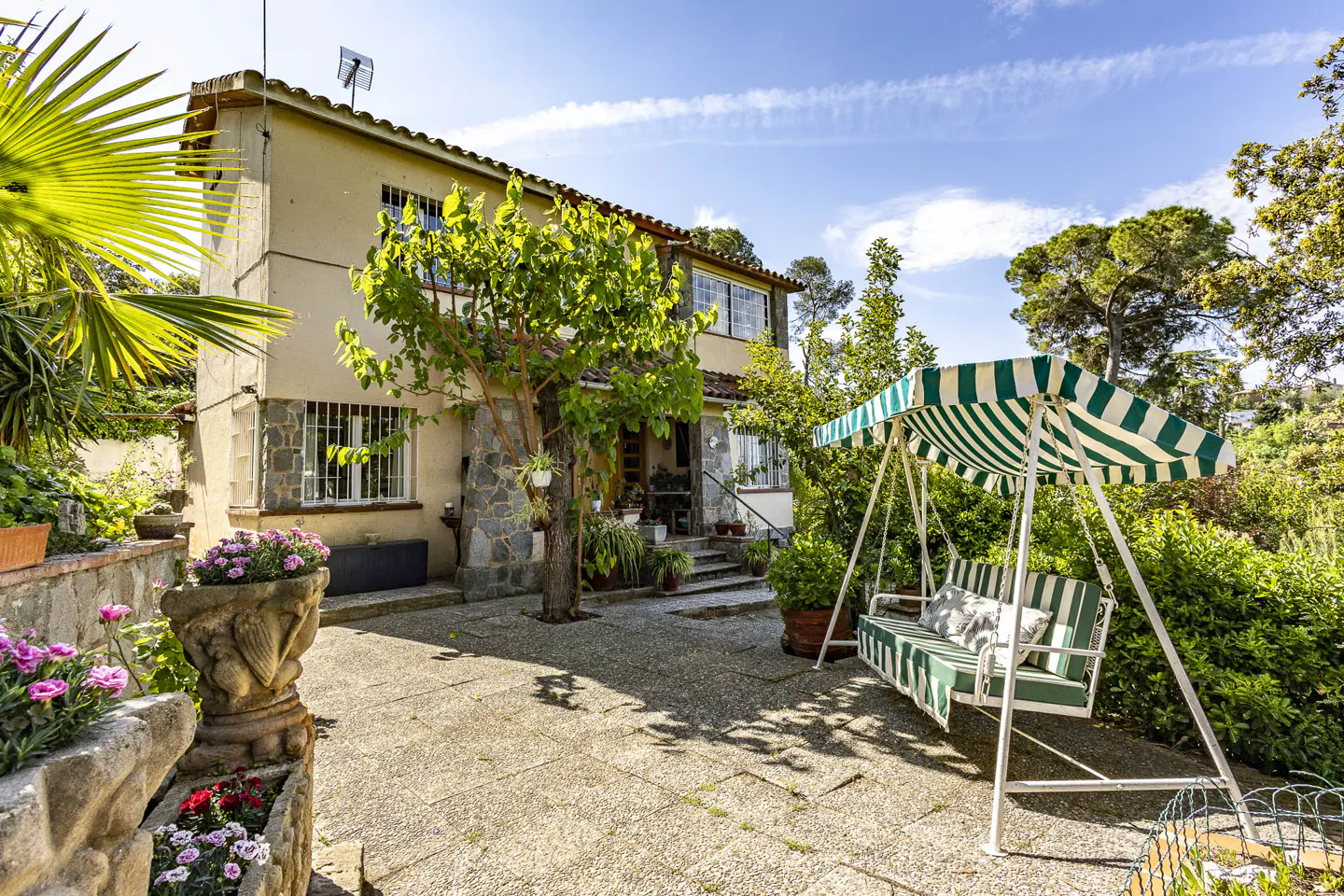 Exterior view of a two-story house with a swing and a stone patio. The swing has green and white stripes.