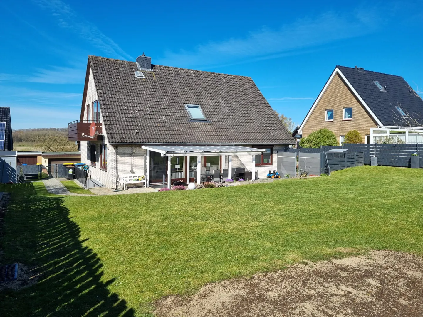 A white brick house with a brown roof and a green lawn under a blue sky.