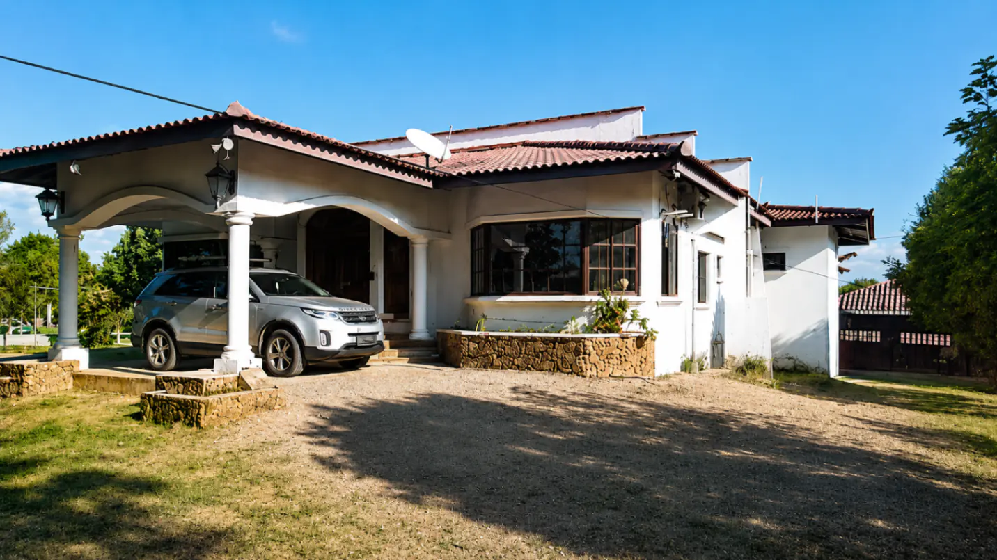 A white house with a red tile roof and a silver SUV parked under a covered carport.