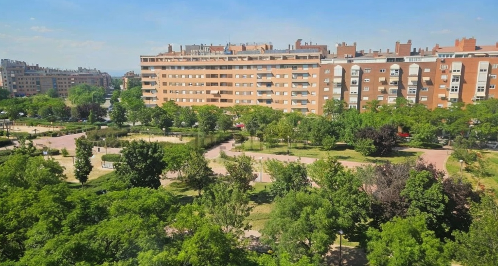 High-angle view of a lush green park with walking paths, surrounded by large, multi-story brick apartment buildings. [AI-generated text]
