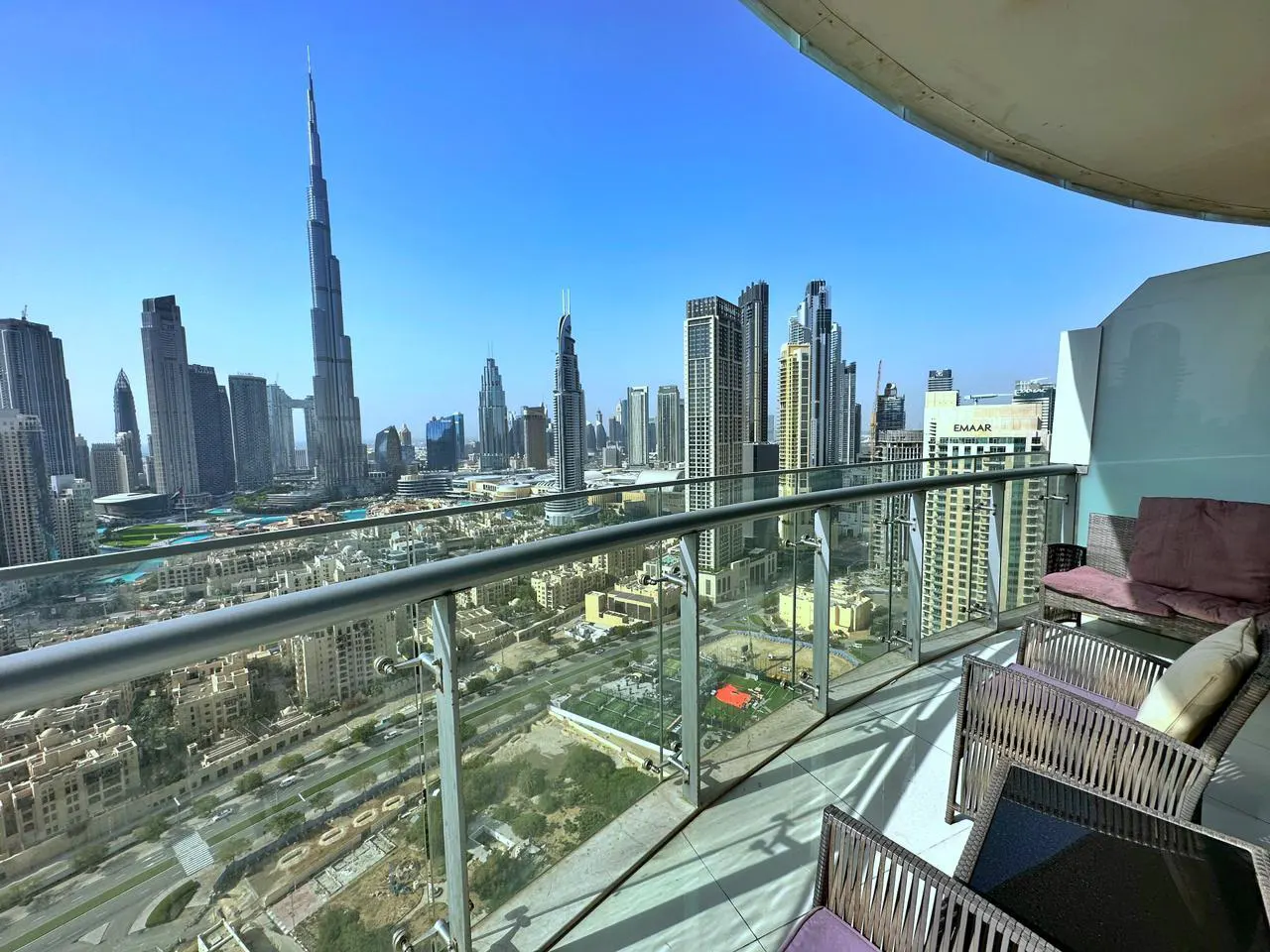 Balcony view of Dubai skyline with Burj Khalifa. Wicker chairs and glass railing overlook the city on a sunny day.