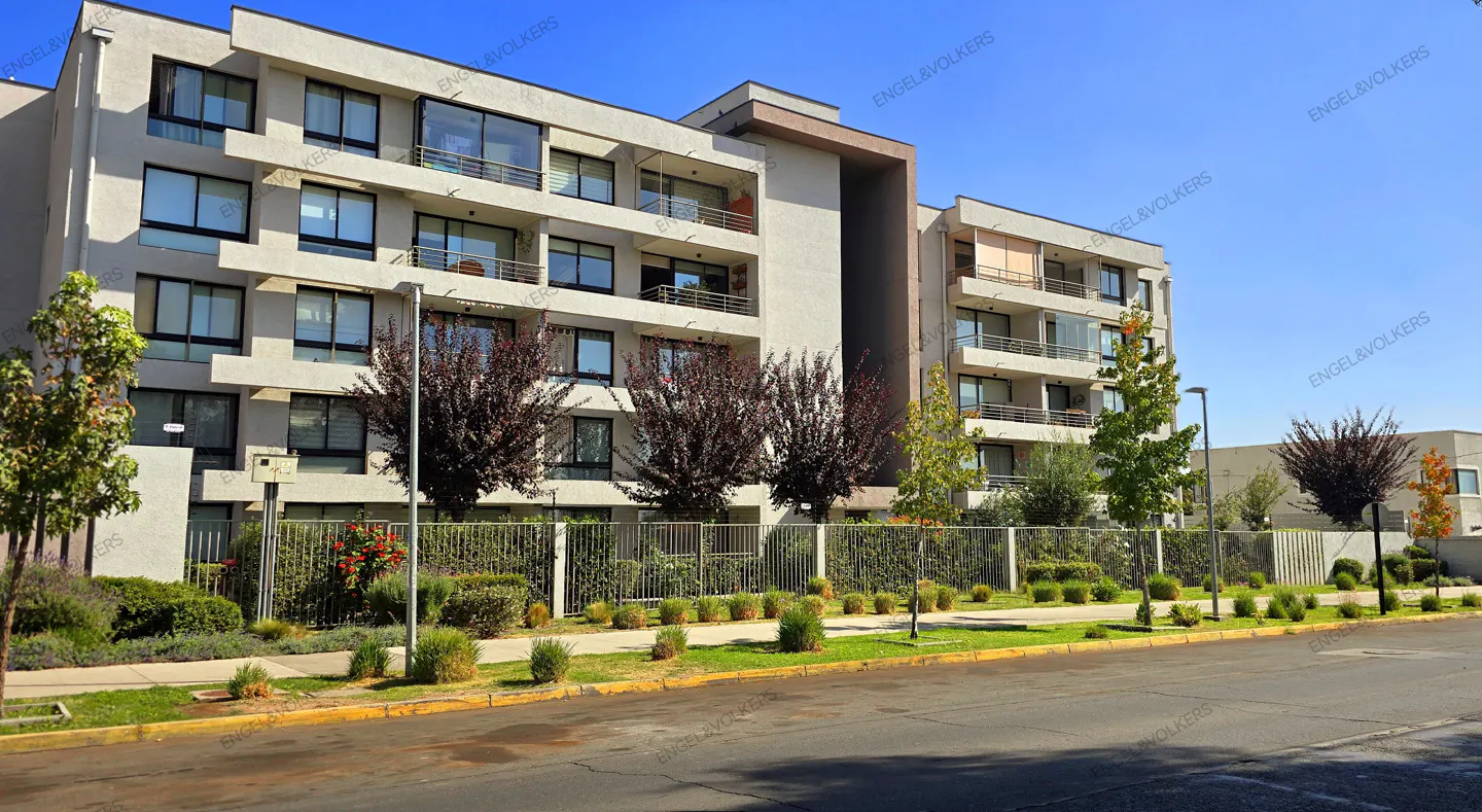 Exterior view of a modern, multi-story apartment building with balconies, trees, and a blue sky.