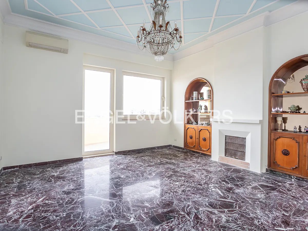 A spacious room with marble floors, white walls, and a blue patterned ceiling with a chandelier.