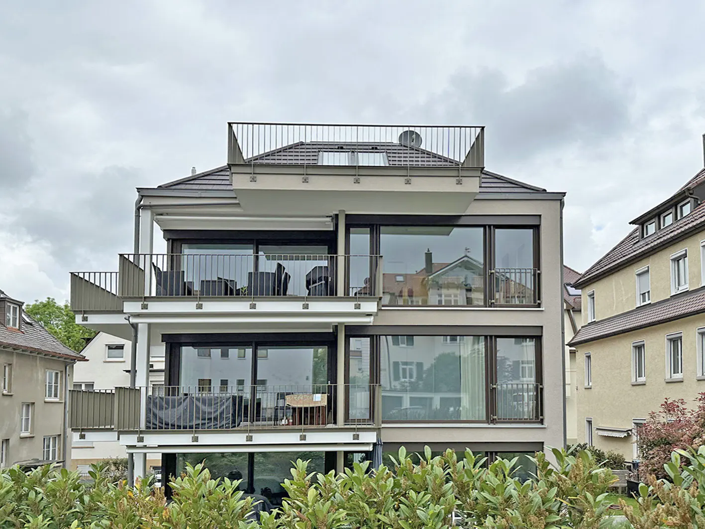 Three-story apartment building with balconies and large windows on a cloudy day.