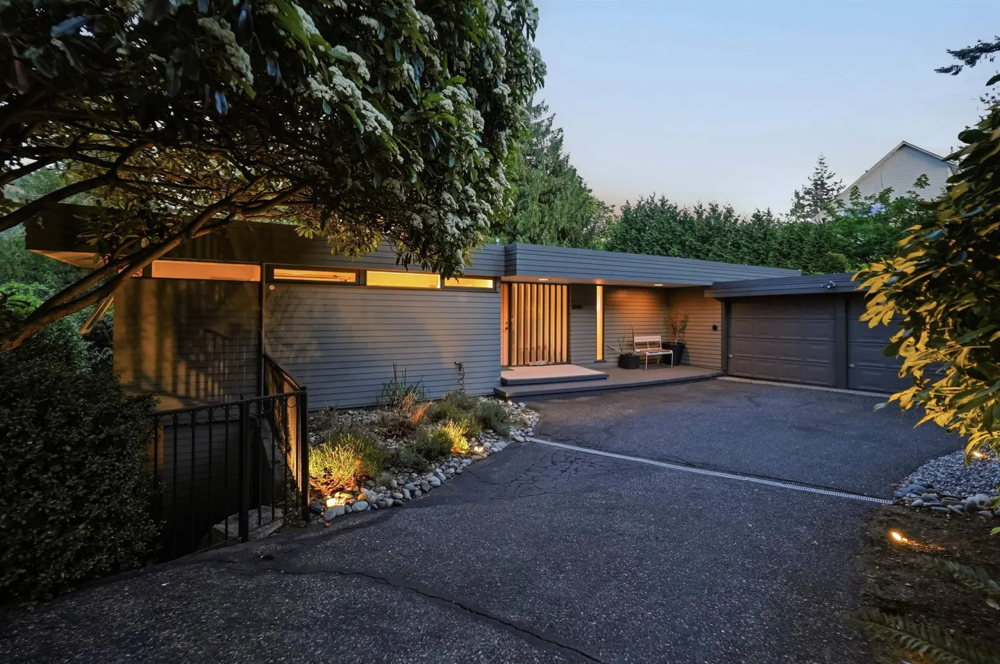 Modern single-story home with gray siding, a dark gray roof, and a matching garage. A tree with white flowers is on the left.