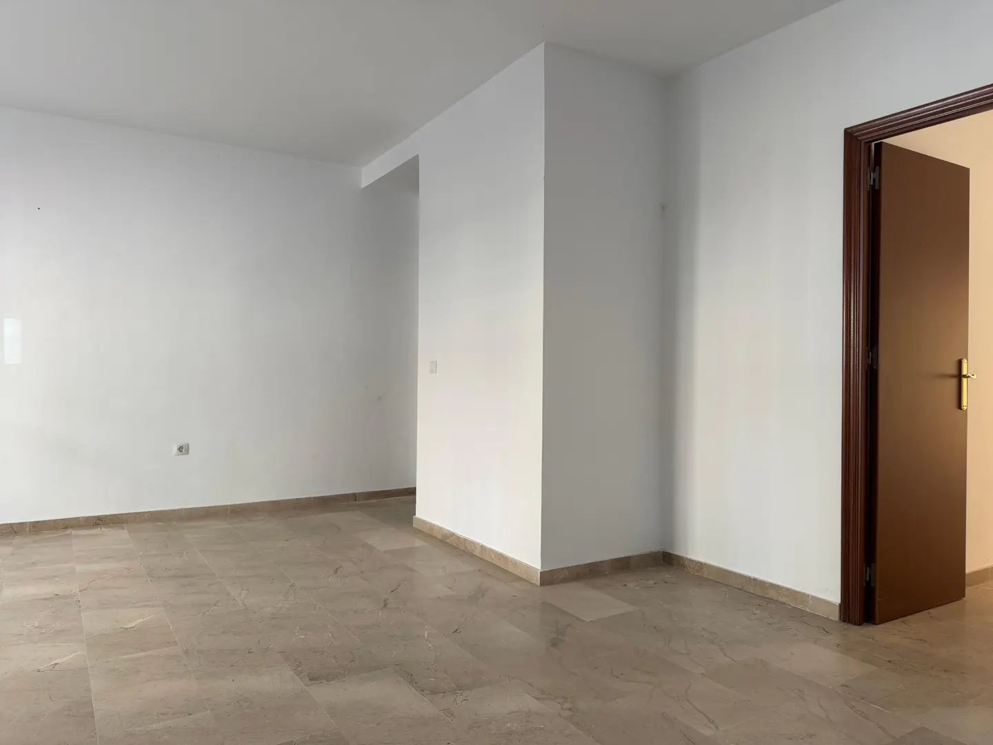 An empty room with white walls, a marble floor, and a brown door slightly ajar.