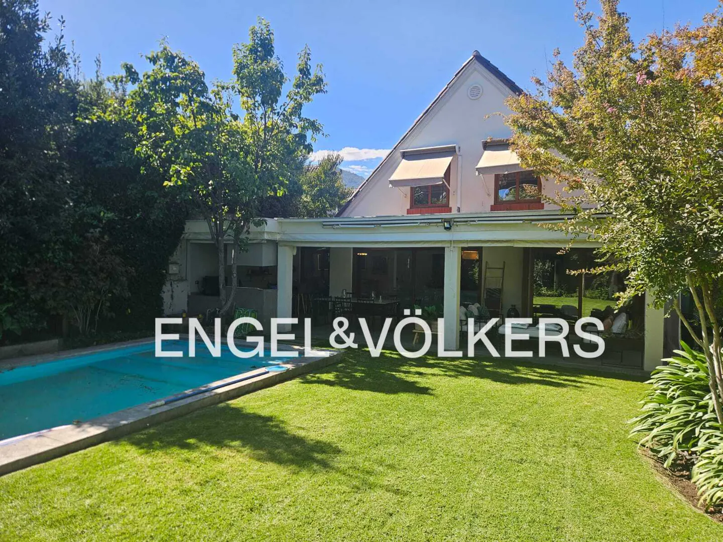 Exterior view of a two-story house with a pool and green lawn, under a blue sky. The Engel & Völkers logo is superimposed on the image.