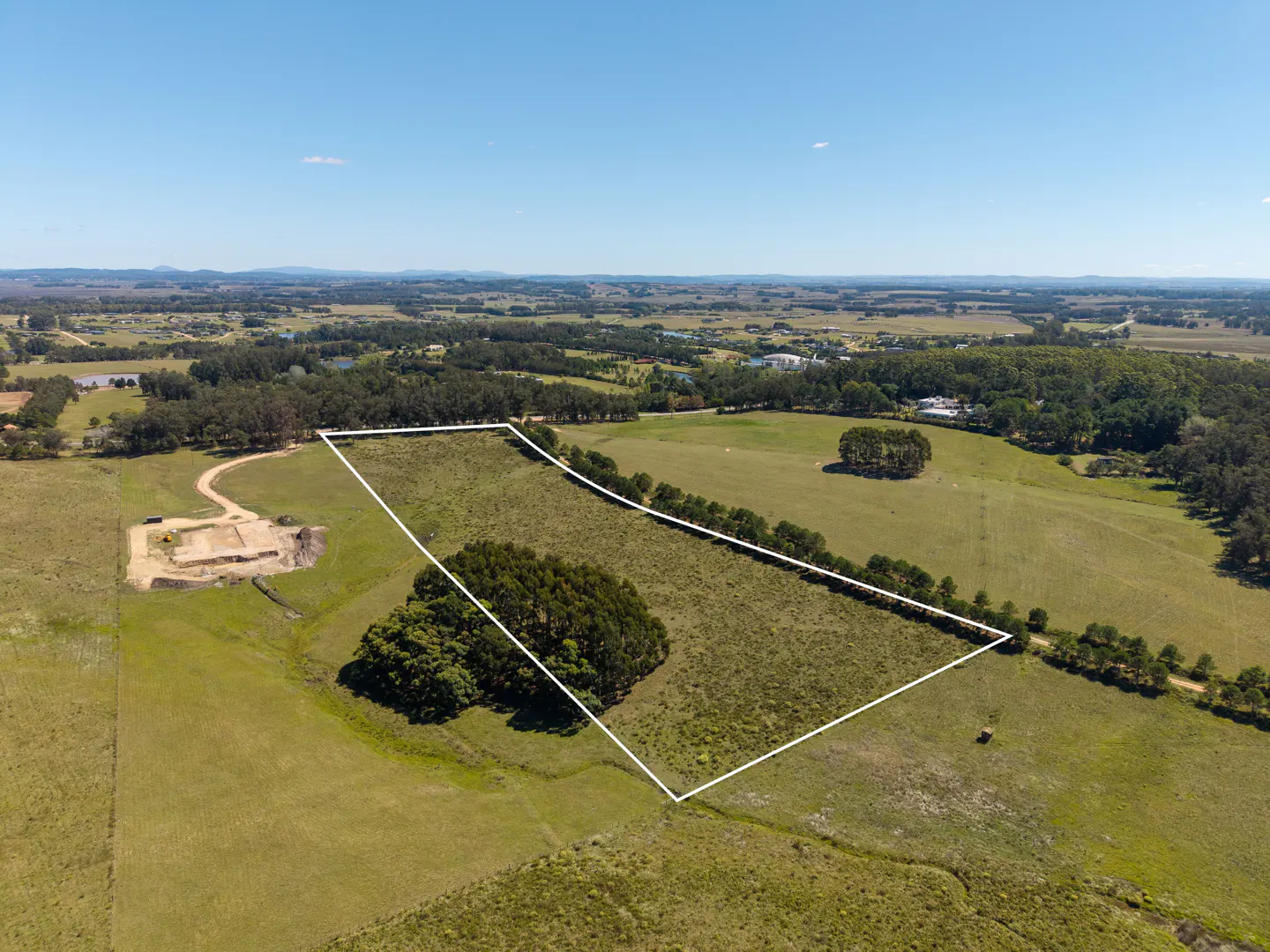 Aerial view of a large, grassy property outlined in white, with trees, fields, and a blue sky.
