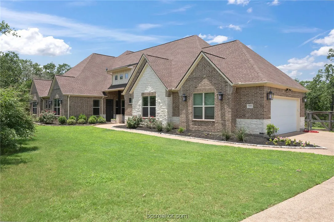 A large, two-story brick house with a brown roof and a green lawn on a sunny day.
