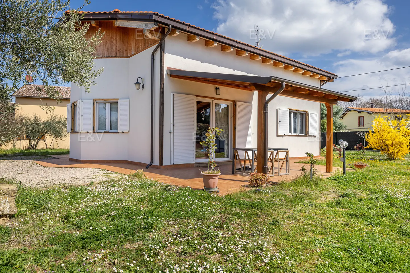 Exterior view of a one-story white house with a brown roof and a green lawn with white flowers.