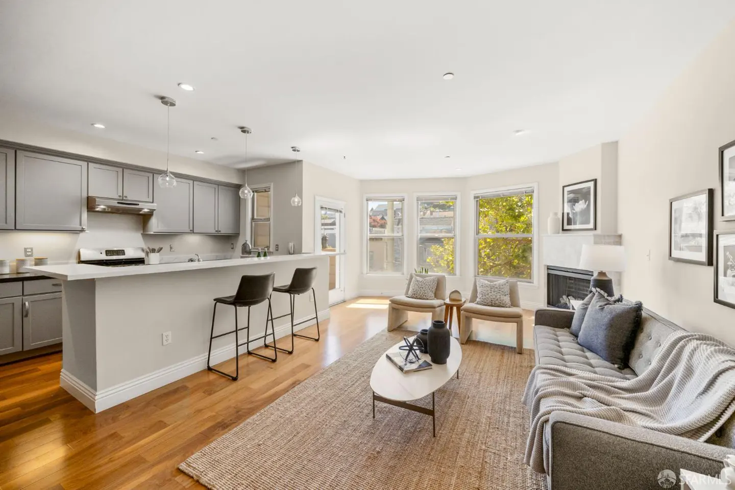 Open-concept living room with gray kitchen cabinets, breakfast bar, two armchairs, and a gray sofa on a jute rug.