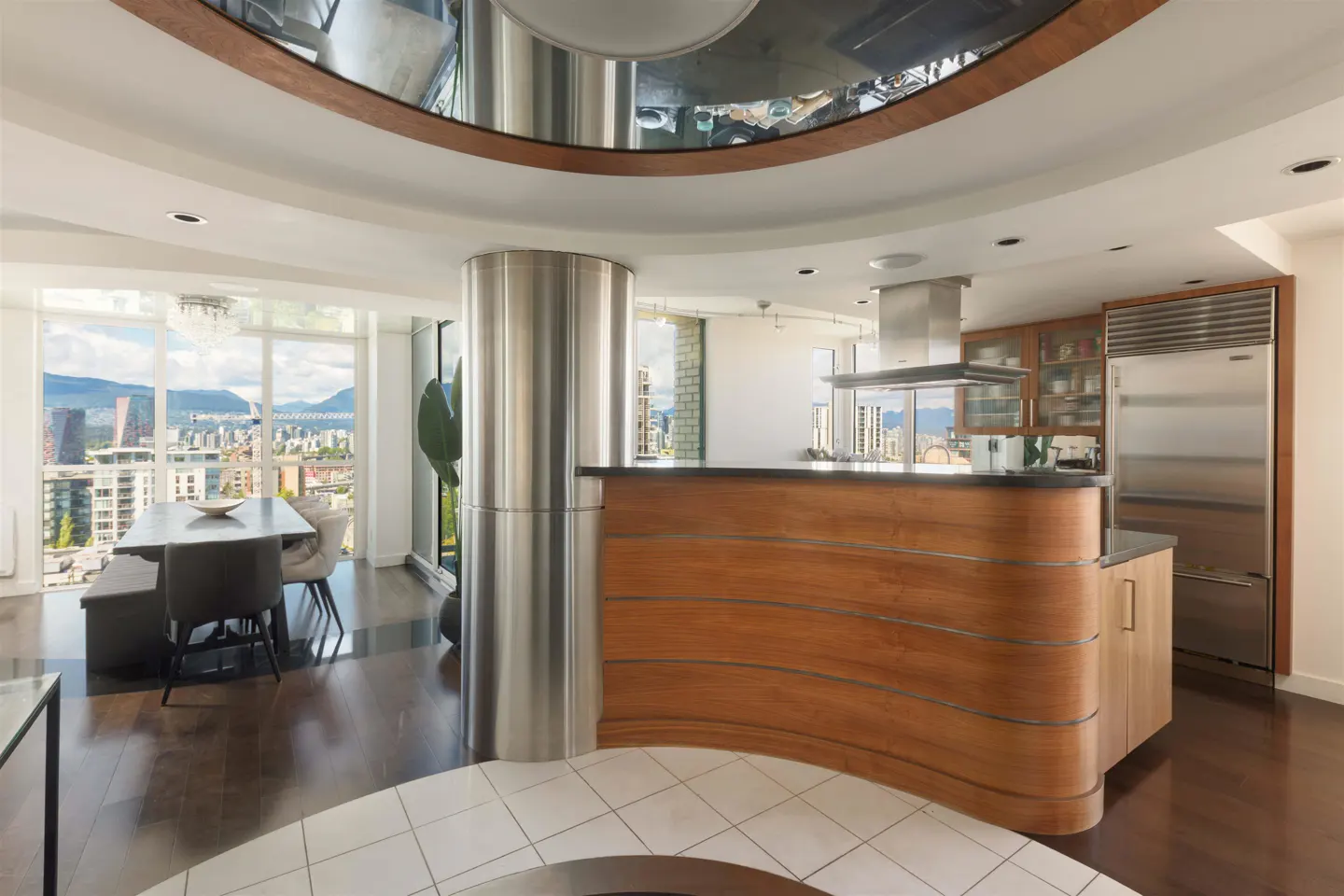 Open-concept condo with wood floors, a curved wood kitchen island, and a dining area with city views.