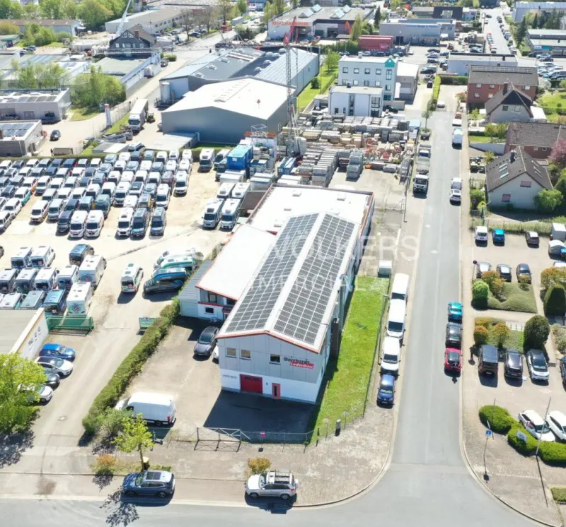 Aerial view of a commercial property with solar panels, surrounded by parked vehicles and industrial buildings.